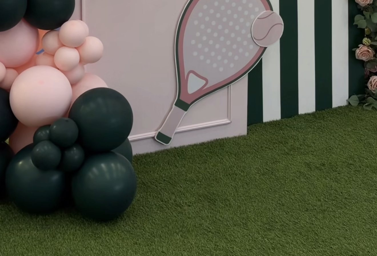 Pink padel racket display beside green and white striped wall